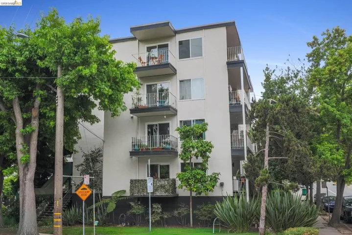 Multi-story building featuring light-colored exterior siding, multiple private balconies with white railings, and sliding glass doors
