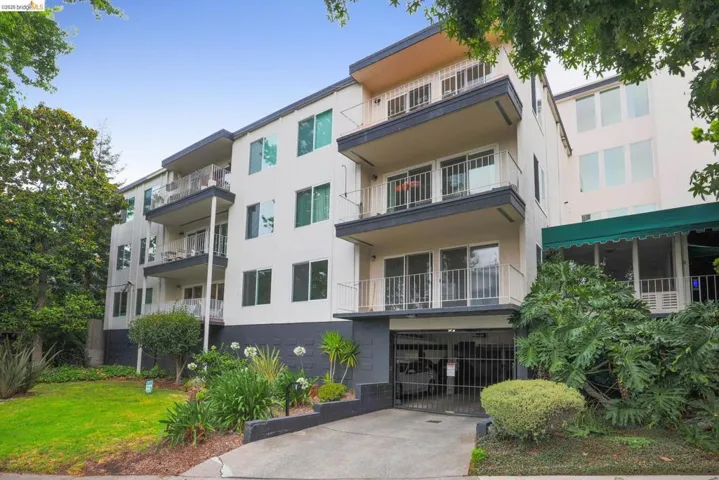 Multi-story building featuring multiple private balconies, a gated subterranean parking garage, and mature perimeter landscaping