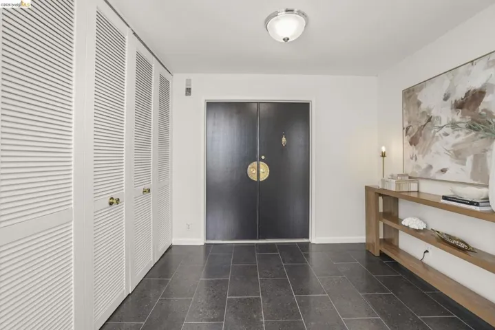 Entryway featuring dark double doors with brass hardware, slate tile flooring, white louvered bifold closet doors with brass knobs, and a ceiling-mounted semi-flush light fixture