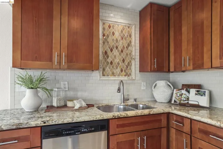 Kitchen featuring wood cabinetry, granite countertops, a stainless steel double basin sink with a pull-down faucet, and a subway tile backsplash