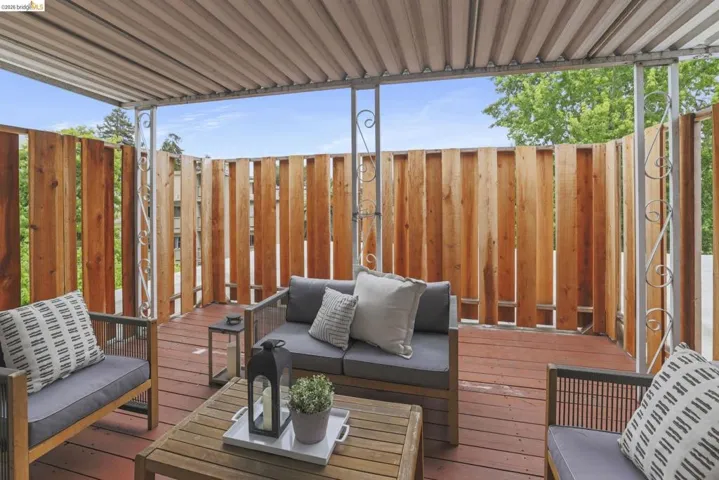Covered outdoor deck featuring a wood-finish floor and slatted wood privacy fence