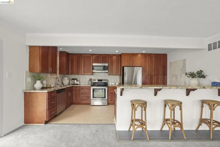 Kitchen featuring wood cabinetry, stainless steel appliances, a light-toned tile backsplash, and granite countertops