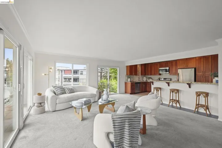 Bright living area featuring light gray carpeting, crown molding, and two sets of sliding glass doors opening to outdoor spaces