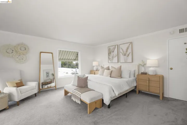 Spacious room with light gray carpeting, crisp white walls, crown molding, and a window featuring a white awning