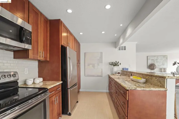 Kitchen featuring stainless steel appliances, rich wood cabinetry, granite countertops, and a subway tile backsplash