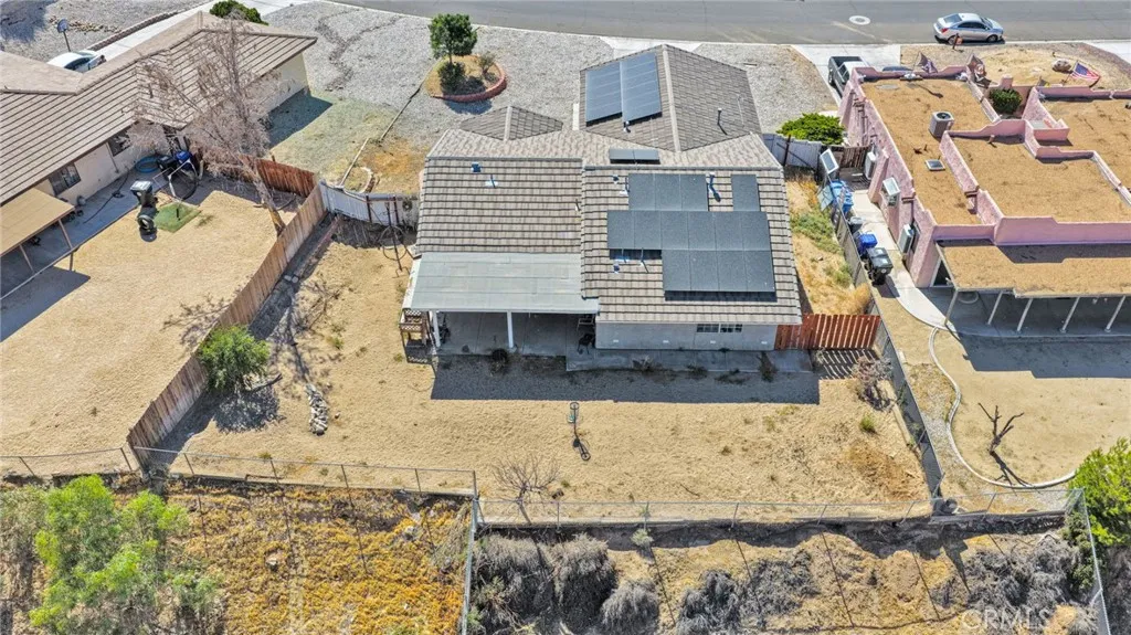Elevated rear aerial view highlighting the massive, fully fenced backyard lot footprint, the solid patio cover, and the extensive rooftop solar array.