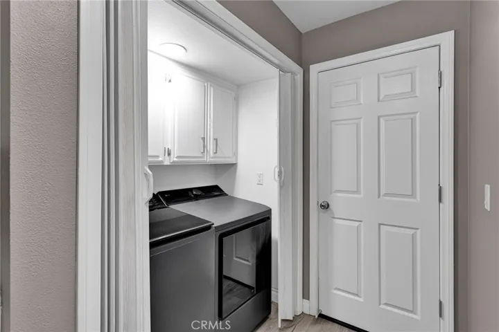 Indoor utility space equipped with modern front-loading laundry machines and clean white overhead storage cabinetry.