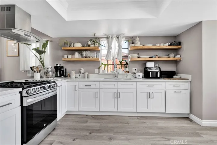 Modern, fully updated kitchen features custom white cabinetry accented with stylish open wood shelving, premium solid-surface countertops, a built-in air-fryer oven, and a sleek glass cooktop vent hood.
