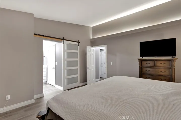Primary retreat highlights premium architectural LED cove drop lighting along the ceiling and a sleek frosted-glass barn door leading to the en-suite bath.