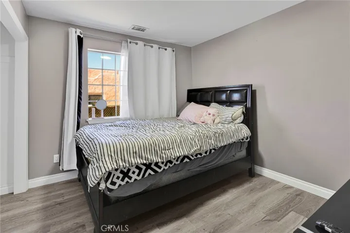 Spacious secondary bedroom featuring continuous wood-look laminate flooring, a large window streaming natural light, and clean gray tones.