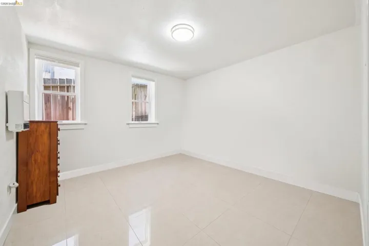 Neutral-toned square tile flooring, white walls, two sash windows, and a flush-mount ceiling light fixture