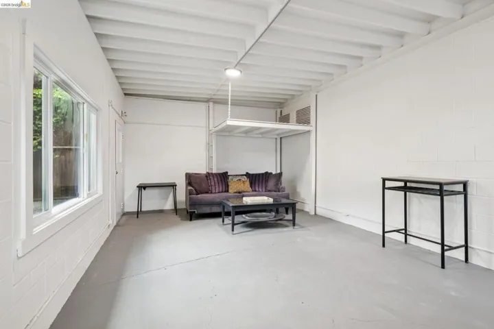 Bright room featuring a large multi-pane window, exposed ceiling joists, white painted block walls, and gray concrete flooring
