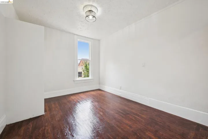 Room featuring wood-finish flooring, a single window, white baseboards, and a circular ceiling light fixture