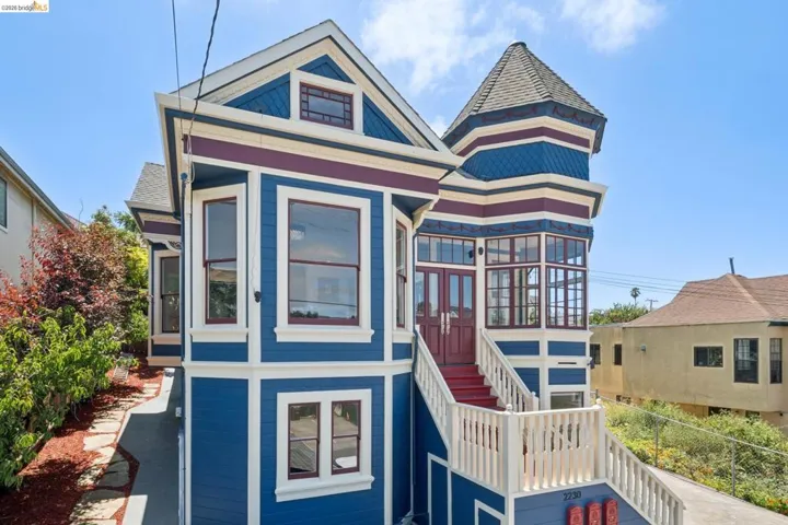 Victorian-style residence featuring a multi-color exterior facade, a prominent turret with a conical roof, and a welcoming red-painted staircase leading to double entry doors