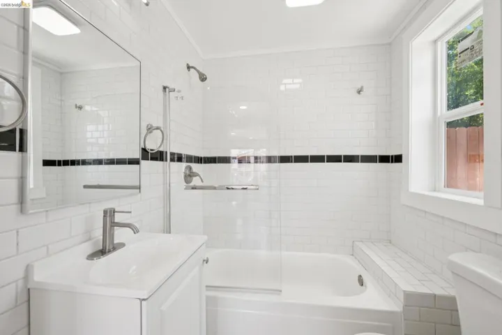 Bathroom featuring white subway tile surround with black accent tile, built-in bathtub, glass shower partition, and a single-pane window