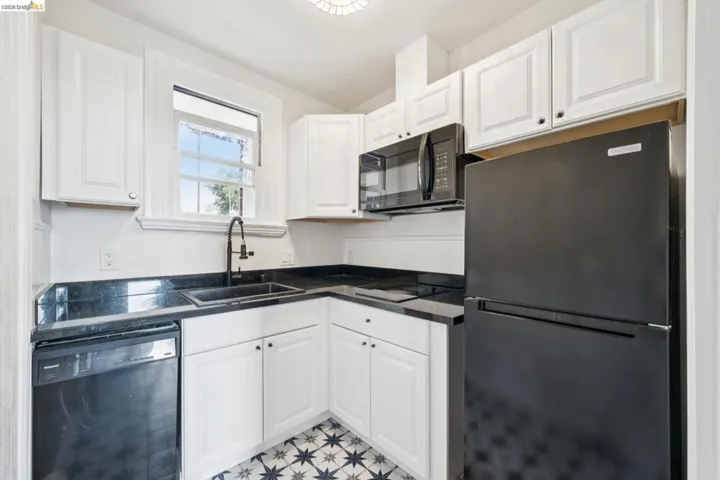 Updated kitchen featuring white shaker cabinetry, dark countertops, a black sink with a matte black faucet, and patterned floor tiles
