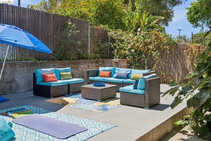 Tiered concrete patio featuring an expansive lounging area, a privacy fence, a concrete block retaining wall, and mature foliage