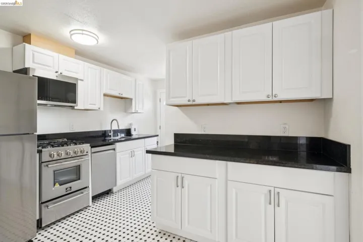 Kitchen featuring black and white patterned floor tile, white shaker-style cabinetry, dark countertops, and stainless steel appliances