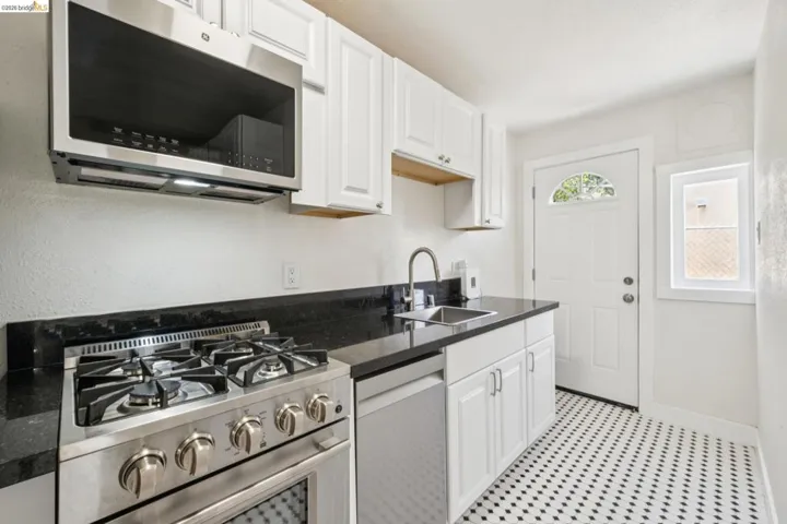 Modern kitchen featuring stainless steel appliances, black countertops, white cabinetry, a single basin sink, and black and white patterned floor tiling