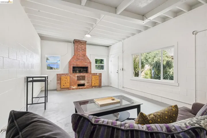 Spacious interior featuring a brick fireplace with wood-paneled accents, exposed beam ceiling, concrete block walls, and multiple windows