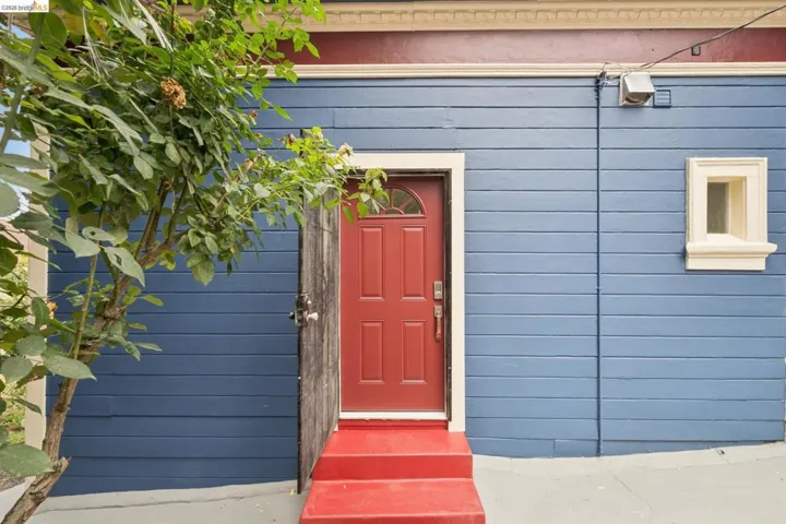 Blue horizontal siding facade with a red entry door, a matching red two-step entry, and a small casement window