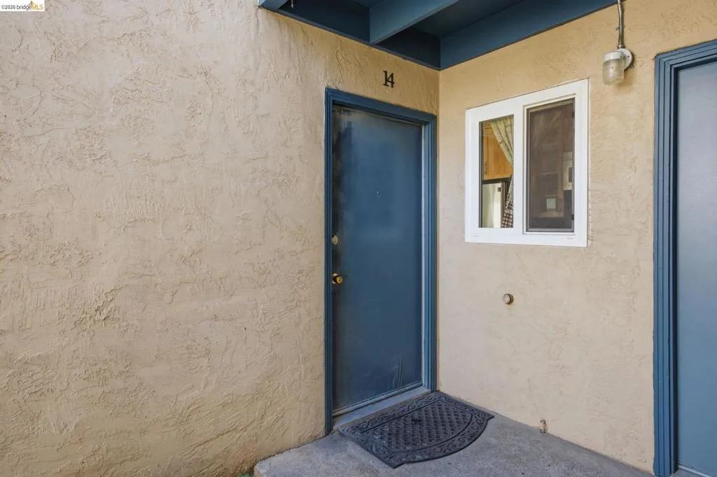 Stucco exterior with a blue entry door, white-framed window, and overhead lighting fixture