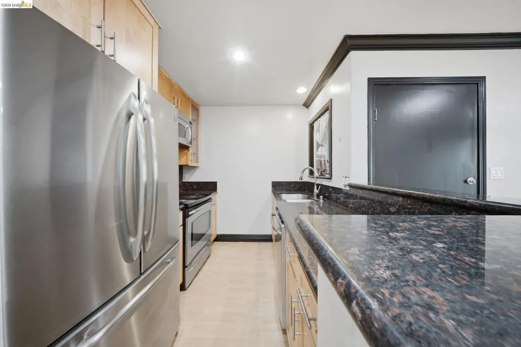 Kitchen featuring stainless steel appliances, dark granite countertops, light wood-finish cabinetry, recessed lighting, and light wood-finish flooring