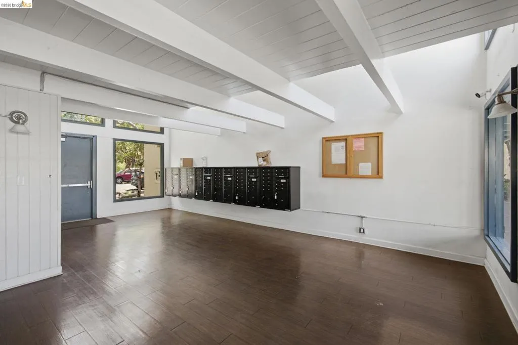 Vaulted ceiling with exposed beams, wood-finish flooring, white shiplap wall accents, large picture window, and transom windows