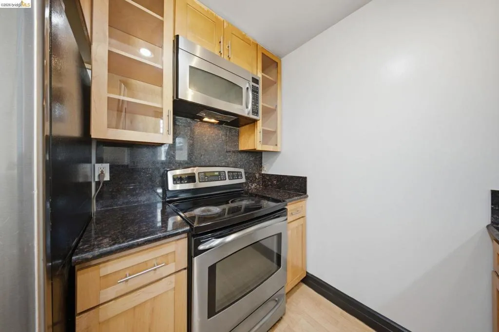 Kitchen area featuring light wood cabinetry, dark stone countertops, a stainless steel range, and a coordinating stainless steel microwave