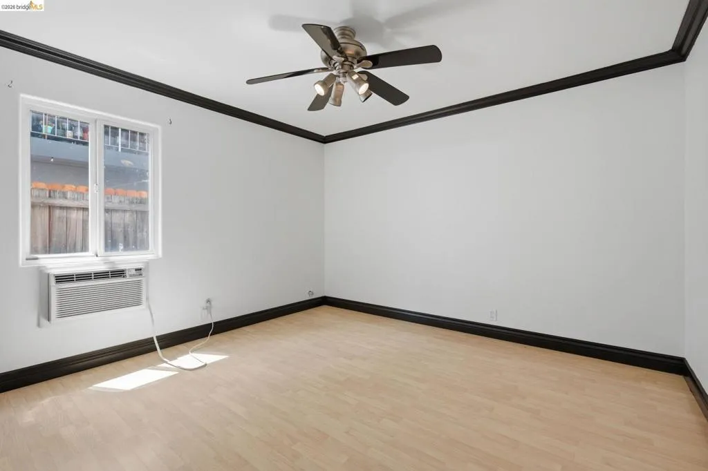 Bright room featuring light wood-finish flooring, a ceiling fan with integrated lighting, and a window air conditioning unit