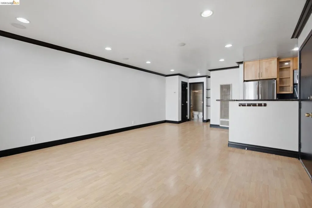 Open-concept living area featuring light wood-finish flooring, recessed lighting, a breakfast bar, stainless steel refrigerator, and wood cabinetry