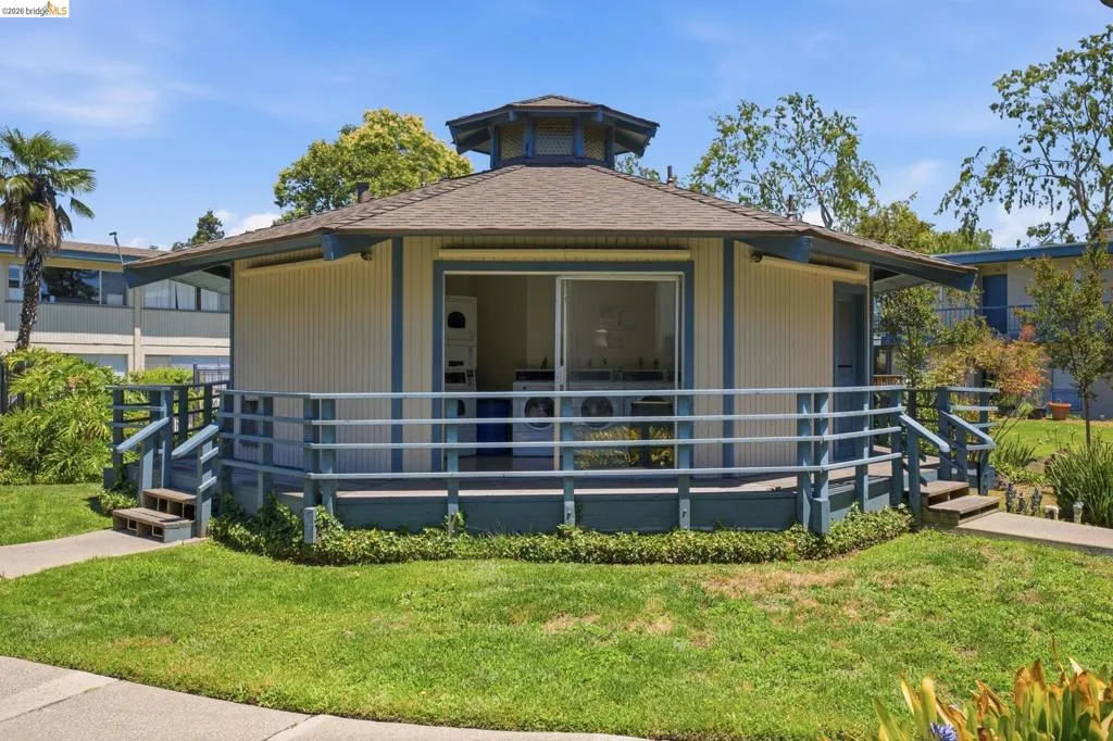 Octagonal building featuring a wrap-around porch with blue railings, a tan exterior with blue trim, and a shingle roof