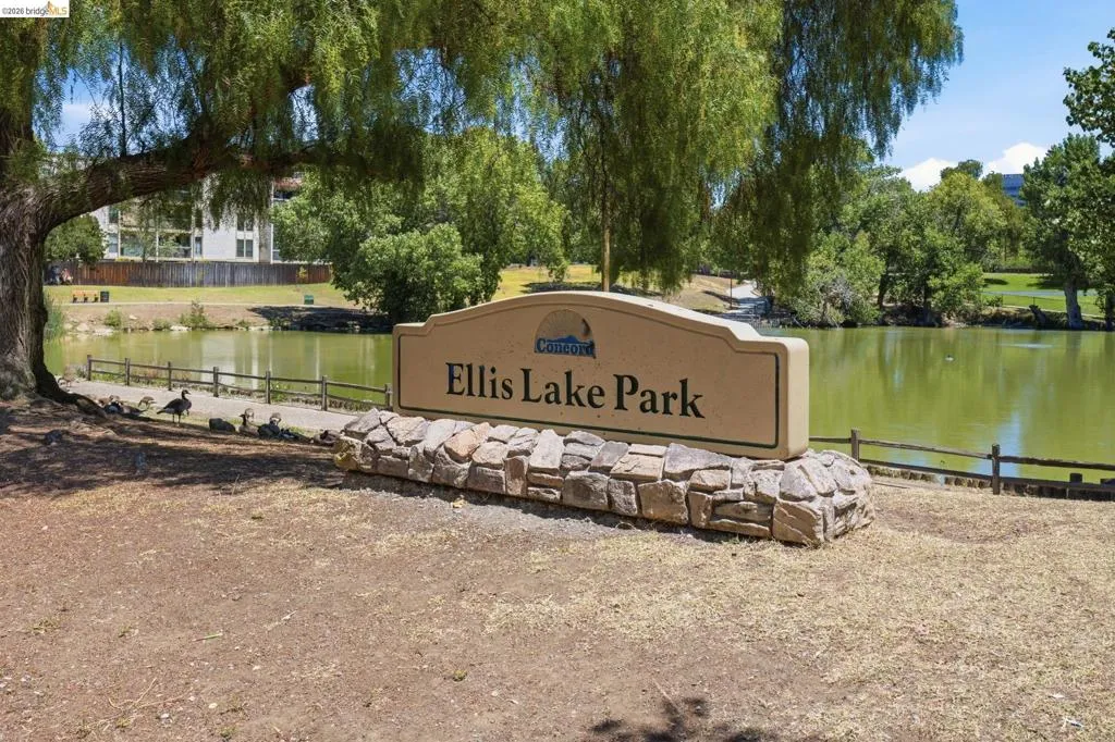 Ellis Lake Park signage with a stone base and a backdrop of mature trees and a body of water