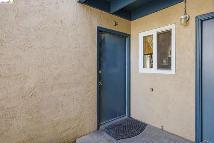Stucco exterior with a blue entry door, white-framed window, and overhead lighting fixture