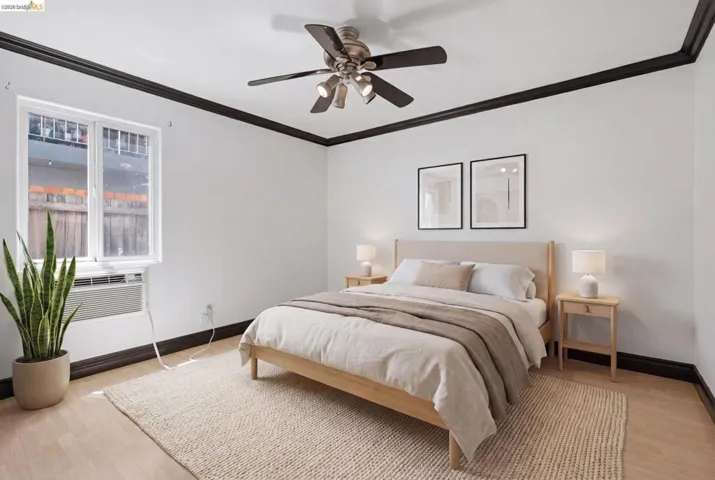 Bedroom featuring light wood-finish flooring, a white window, and a dark-toned ceiling fan