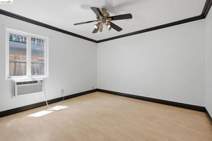 Bright room featuring light wood-finish flooring, a ceiling fan with integrated lighting, and a window air conditioning unit
