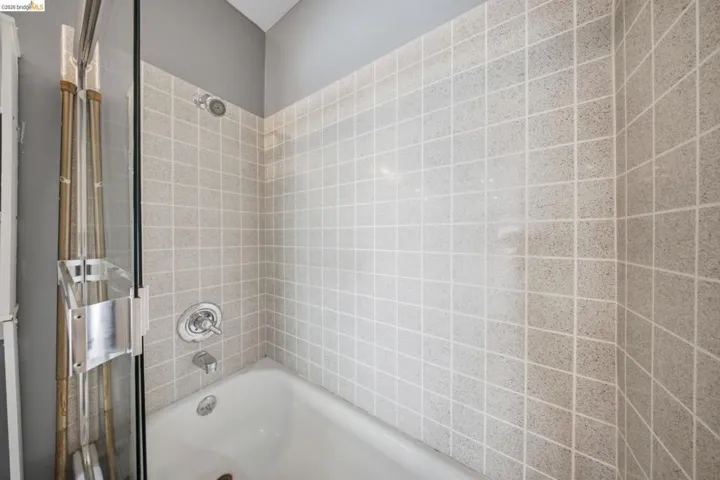 Bathtub with square tile surround, chrome fixtures, and a glass shower door