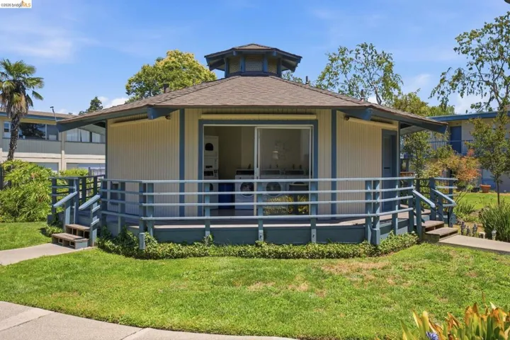 Octagonal building featuring a wrap-around porch with blue railings, a tan exterior with blue trim, and a shingle roof
