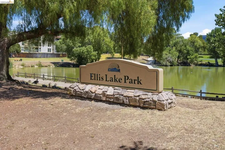 Ellis Lake Park signage with a stone base and a backdrop of mature trees and a body of water