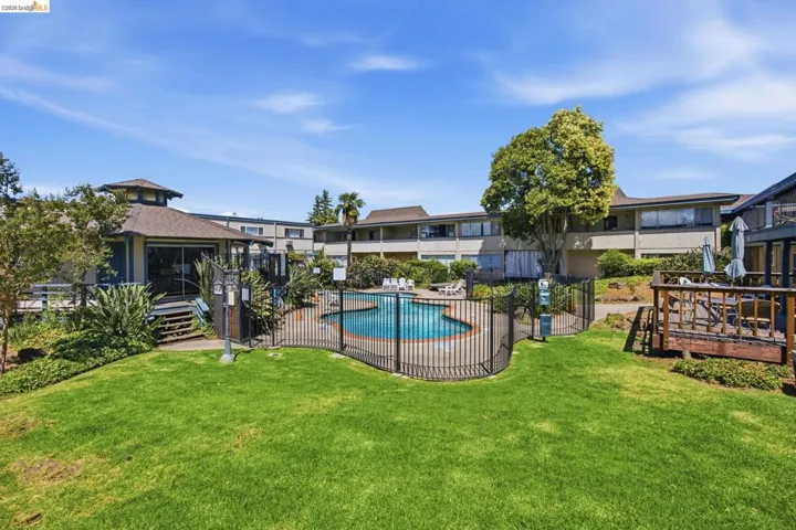 Lush green lawn with a fenced swimming pool, surrounding patio, and a covered pavilion featuring a deck
