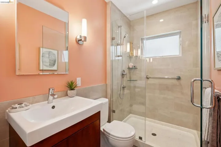 Bathroom featuring a glass-enclosed shower with tile surround, a single vanity with a flat-panel wood cabinet, a wall-mounted mirror, and a toilet