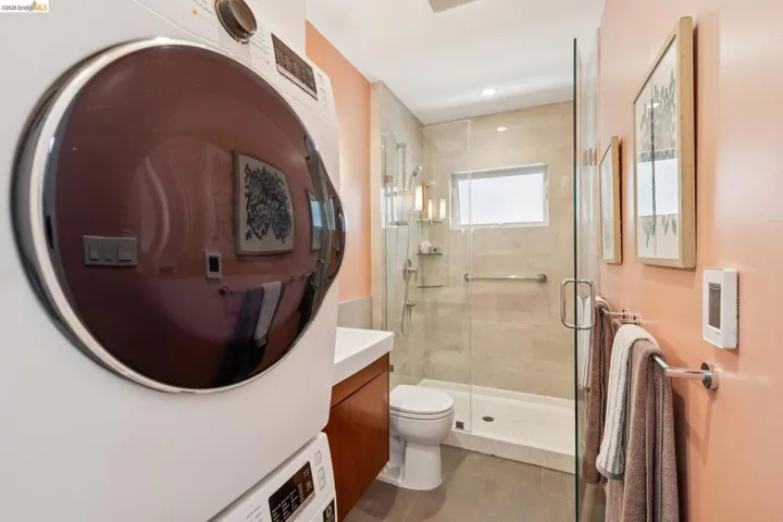 Integrated laundry appliances within a bathroom featuring a walk-in shower with glass enclosure, beige tile surround, and a compact window