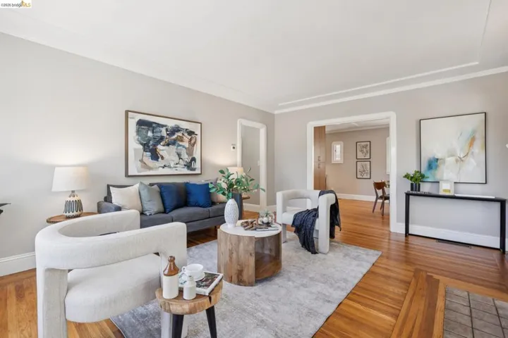 Living area featuring hardwood flooring, light gray wall paint, crown molding, and an open entryway to an additional room