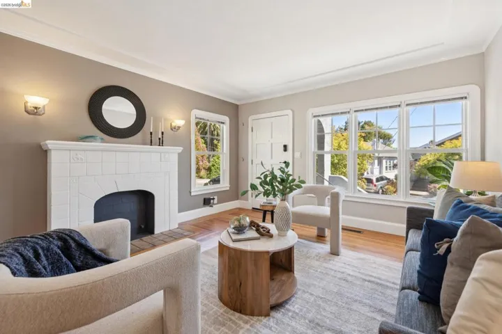 Living area featuring a tiled fireplace with sconce lighting, wood-finish flooring, crown molding, and large windows