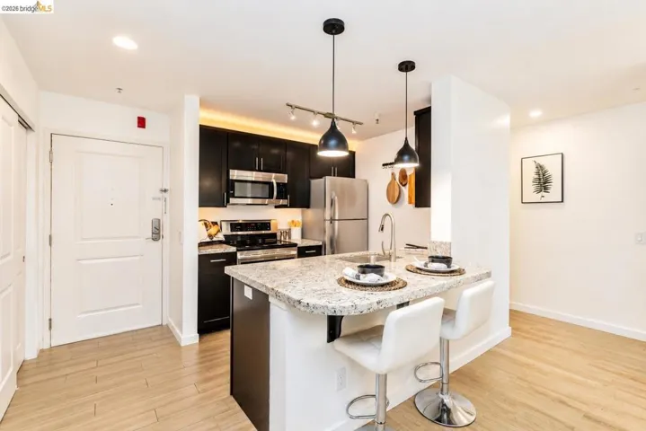 Modern kitchen featuring dark cabinetry, stainless steel appliances, and a light granite countertop with breakfast bar seating
