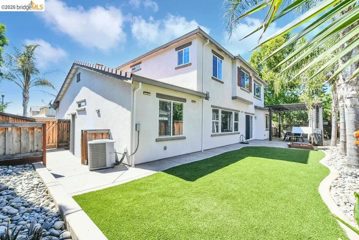 Spacious backyard featuring a large patio, lush artificial turf, and a pergola-covered outdoor dining area