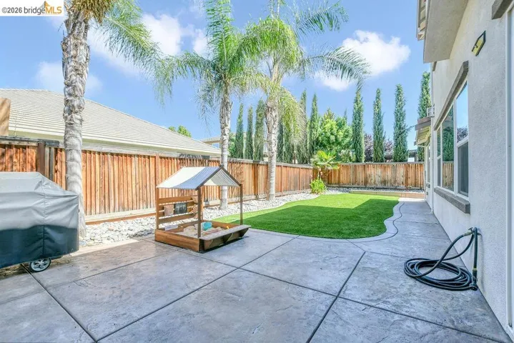 Spacious backyard featuring a stamped concrete patio, artificial turf lawn, privacy fencing, and mature palm trees
