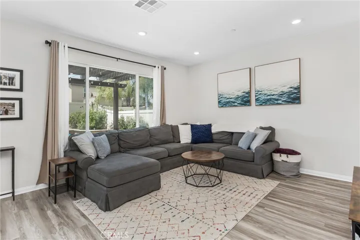 Living room w/ vinyl flooring, large window to view the beautiful back yard and can lighting.