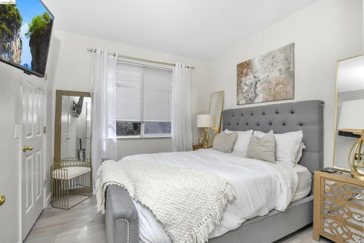 Bedroom featuring neutral wall paint, wood-finish flooring, a window with horizontal blinds and sheer curtains, and a solid core door with brass hardware