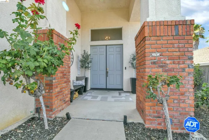 Entryway featuring a double door with transom window, flanked by brick columns and decorative landscaping